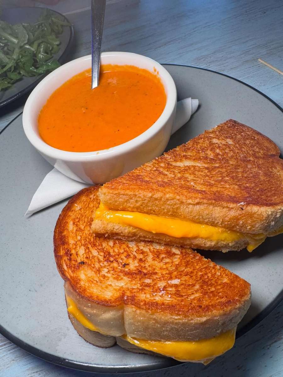 Classic grilled cheese sandwich with melted cheddar cheese served alongside creamy tomato soup
