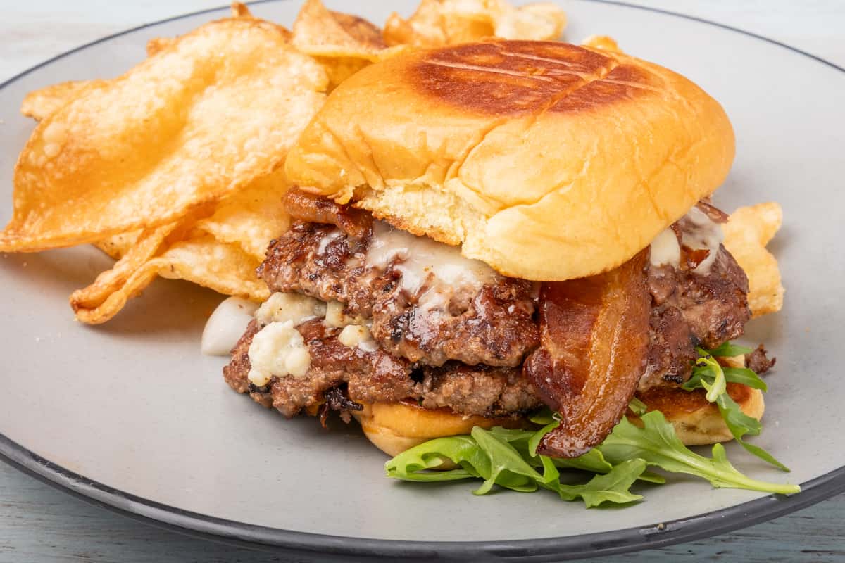 Gruyère cheeseburger topped with crispy bacon on a toasted bun, served with kettle chips at Sharky's NSB, a coastal scratch kitchen and beach bar on Flagler Avenue in New Smyrna Beach.