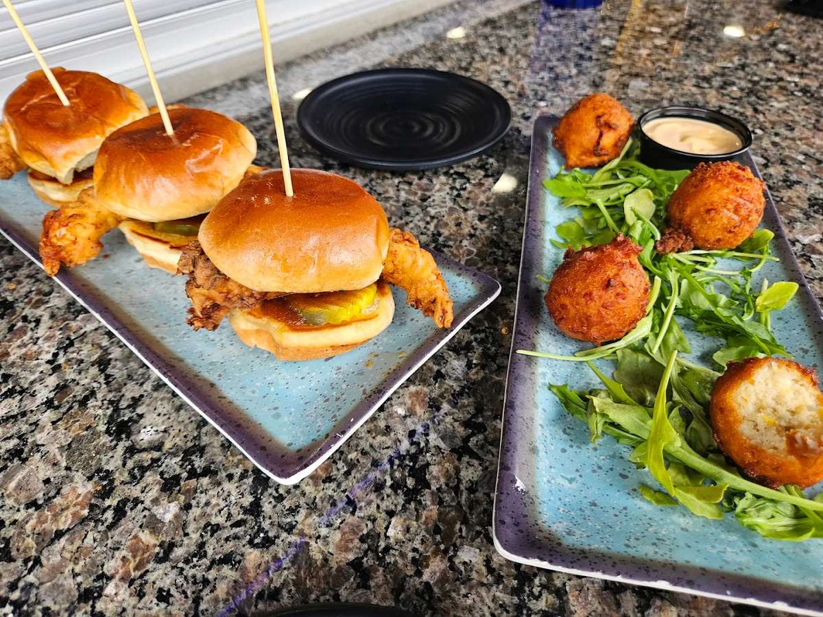 Crispy fried shrimp sliders with pickles on toasted brioche buns served alongside golden hush puppies and creamy dipping sauce