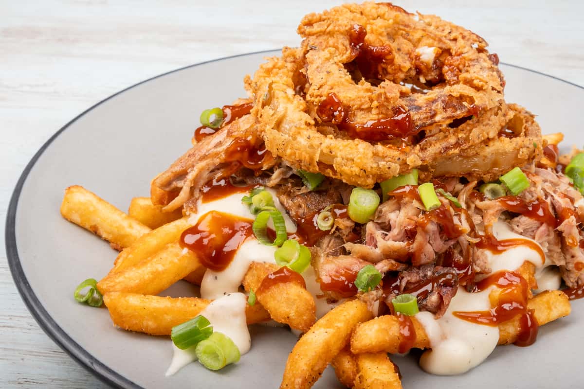 Loaded fries topped with crispy onion straws, cheese sauce, and chopped green onions on a gray plate at a restaurant