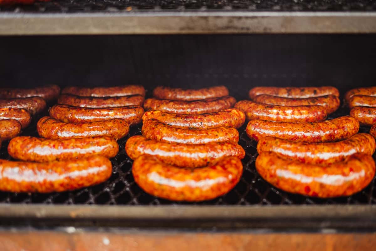Several rows of sausages sit on a grill rack. The sausage texture is semi-smooth and orange, and they look delicious and ready to eat.