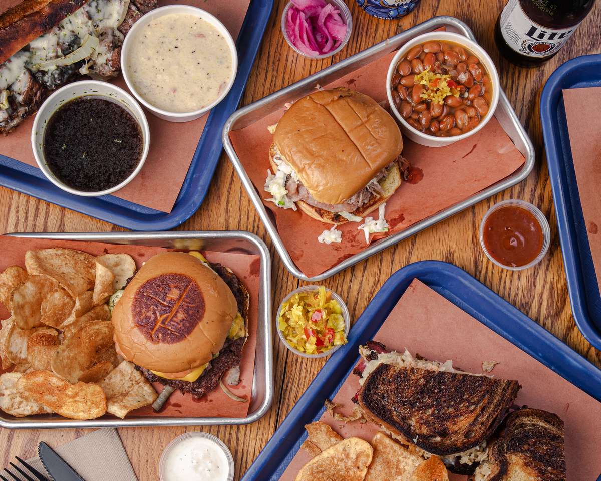A high-angle shot showcases a diverse spread of barbecue dishes arranged on trays. The photo conveys a vibrant culinary experience, perfect for a restaurant's catering page.