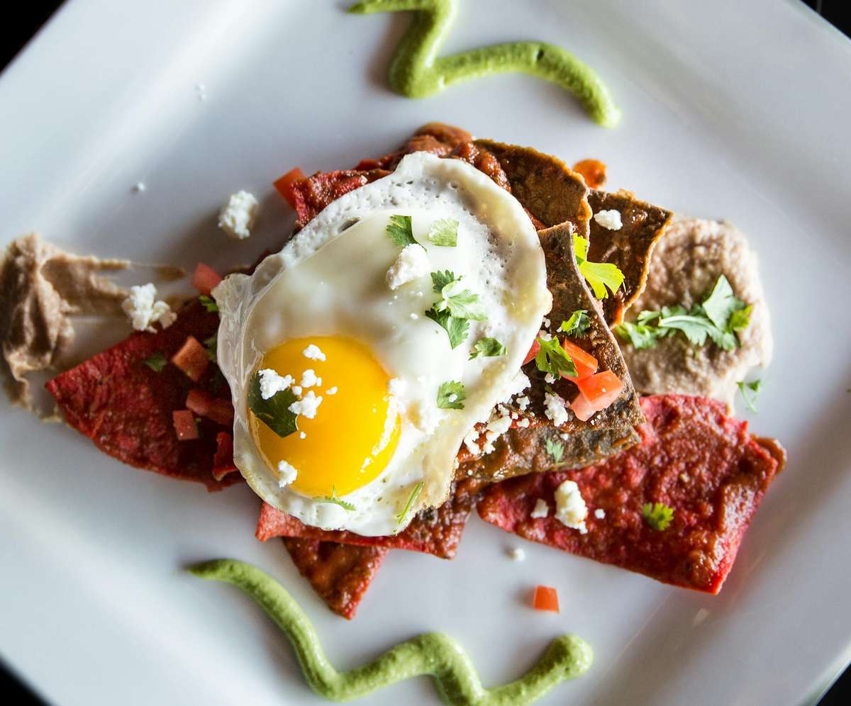 Delicious Mexican chilaquiles topped with a sunny-side-up egg and fresh herbs.