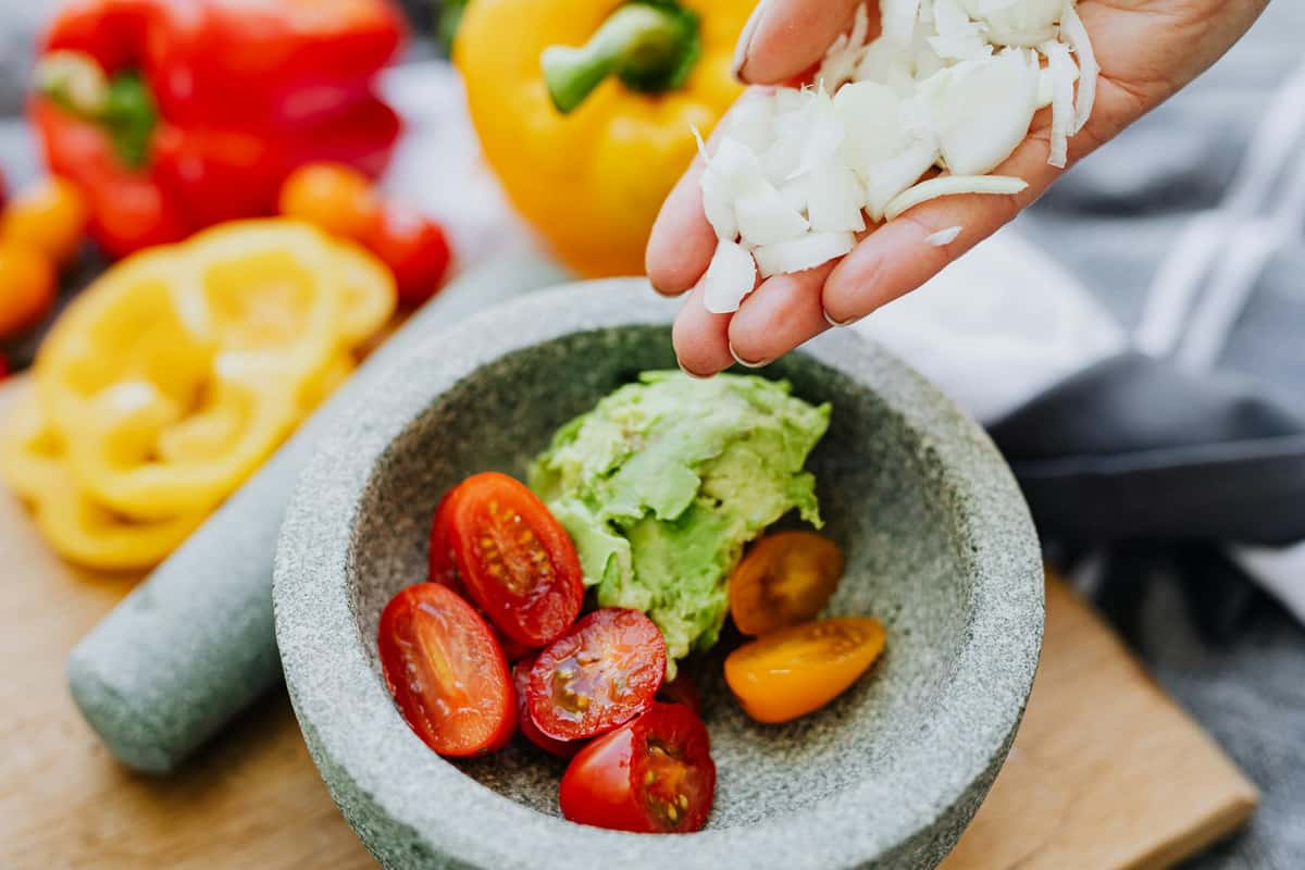 Colorful ingredients like avocados, tomatoes, and onions in a stone mortar for guacamole.