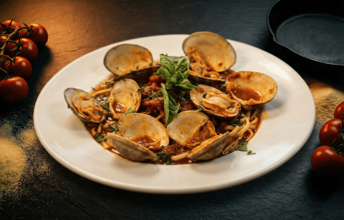 Pasta with clams, tomato sauce, and fresh basil on a white plate.