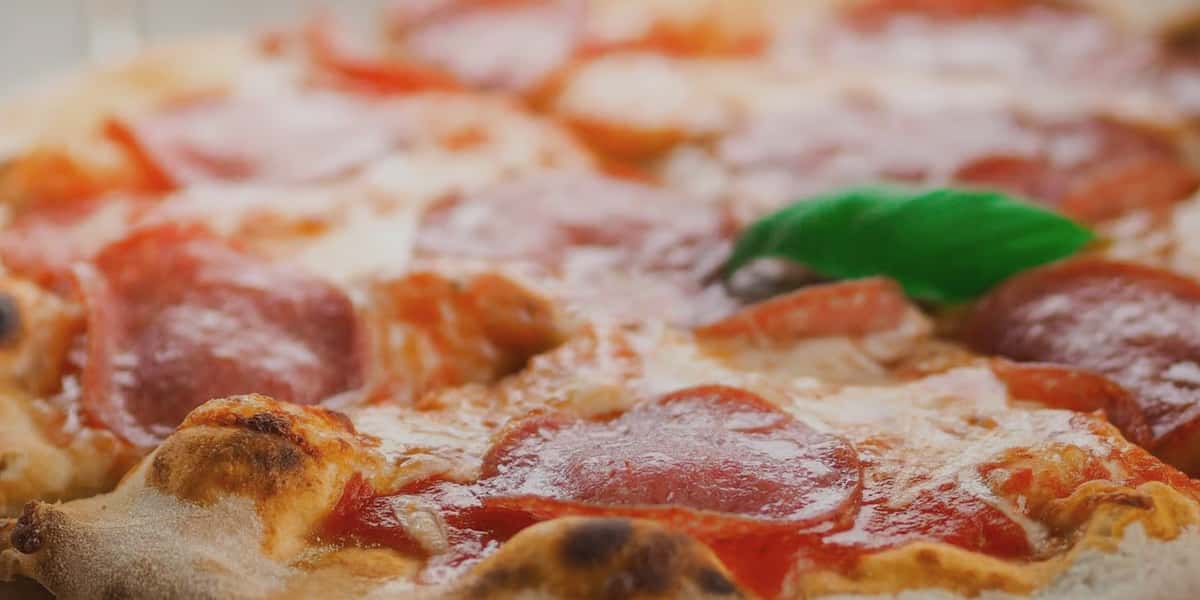 Fresh pepperoni pizza with melted mozzarella, rich tomato sauce, and basil garnish on a blistered artisan crust.