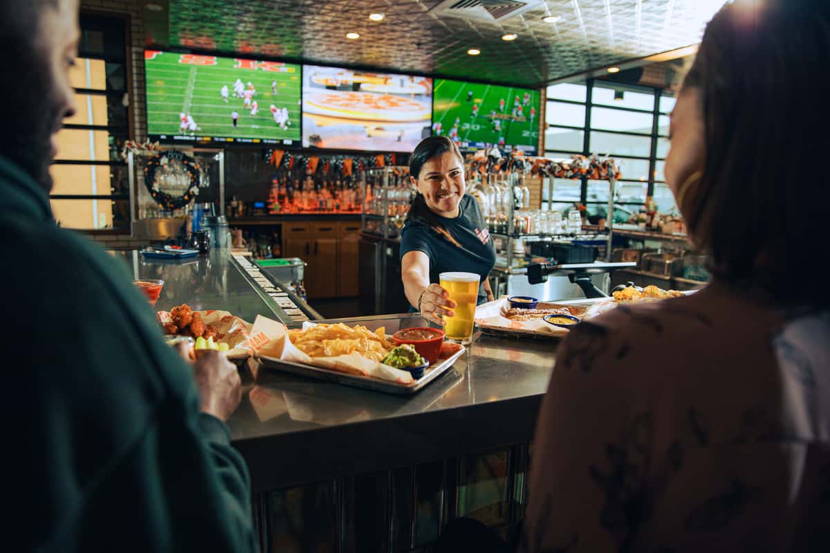 Employee serving guests with football on tv's
