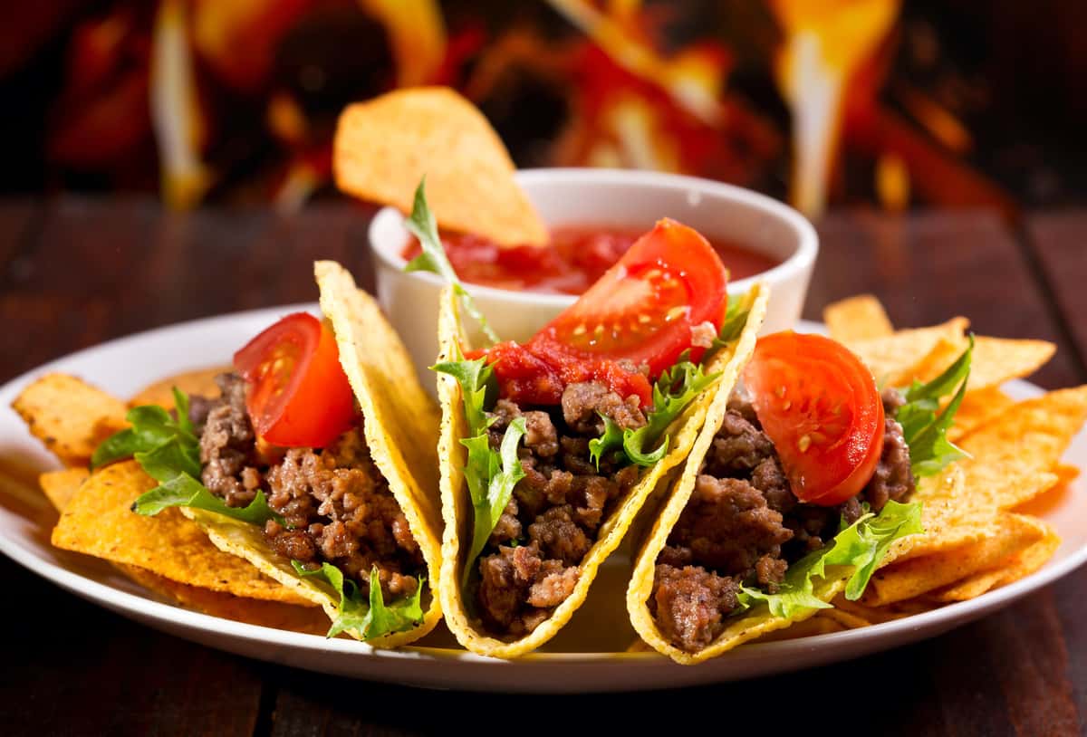 three tacos topped with lettuce and tomato on a plate with sauce on the side