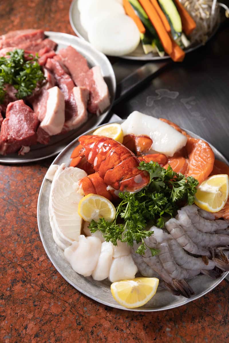 A vibrant platter of assorted sashimi features thick, fresh cuts of raw fish including salmon, tuna, and white fish. The slices are artfully arranged with lemon wedges, parsley, and greens, creating a colorful and appetizing presentation that emphasizes freshness and quality.