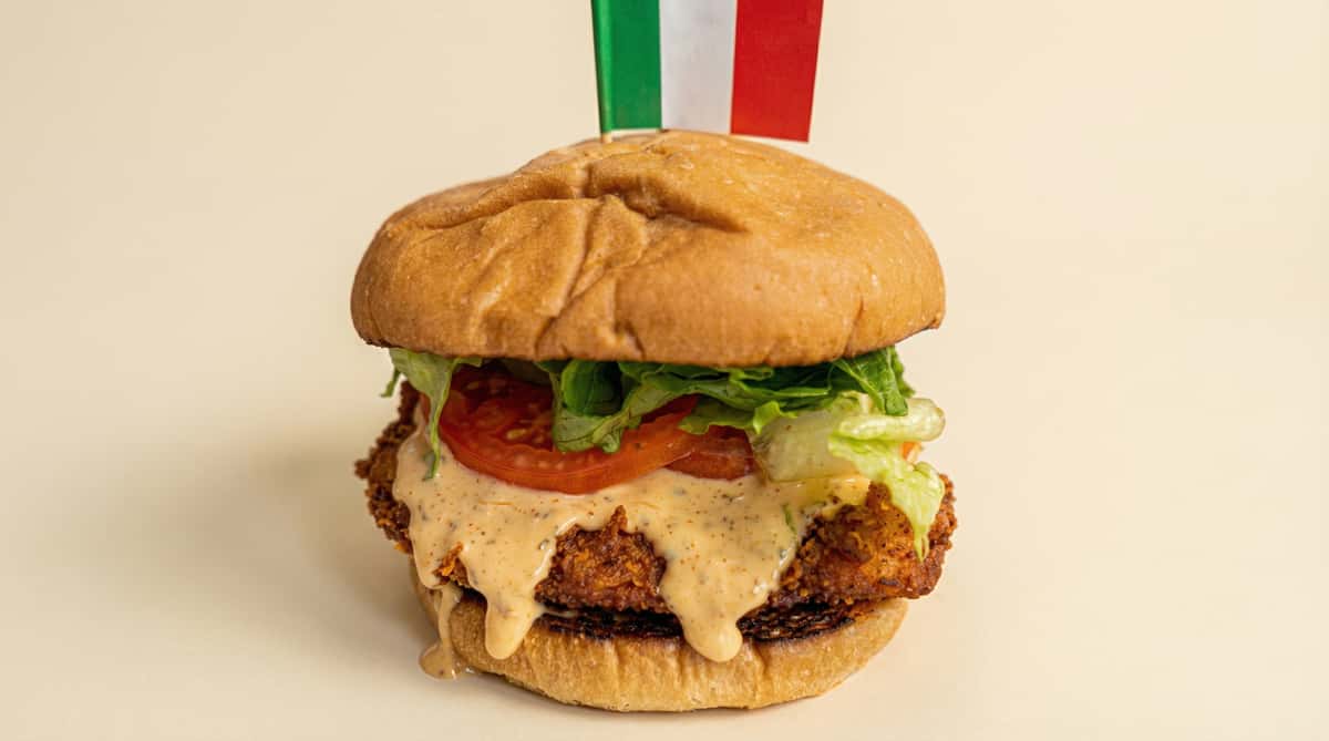 crispy chicken sandwich with lettuce tomato and creamy sauce on a toasted bun with Italian flag pick