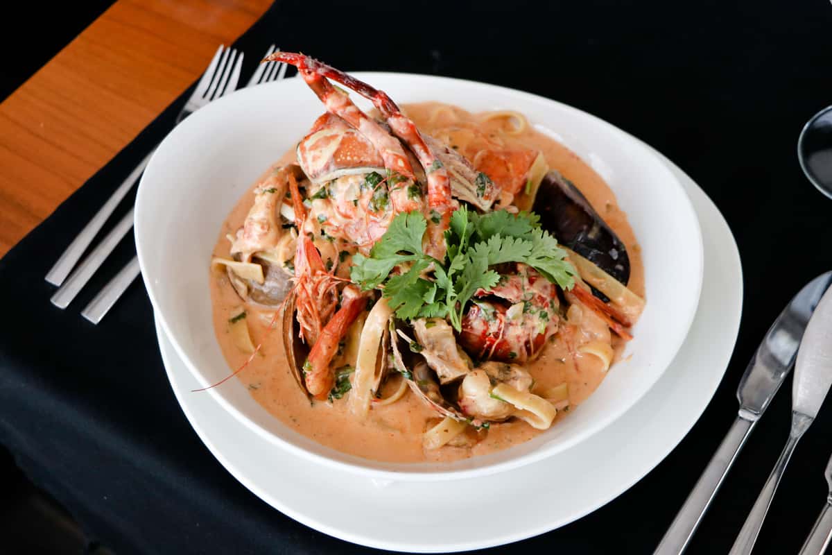 Appetizing seafood pasta in creamy lobster sauce, garnished with fresh herbs, served in a white ceramic bowl.