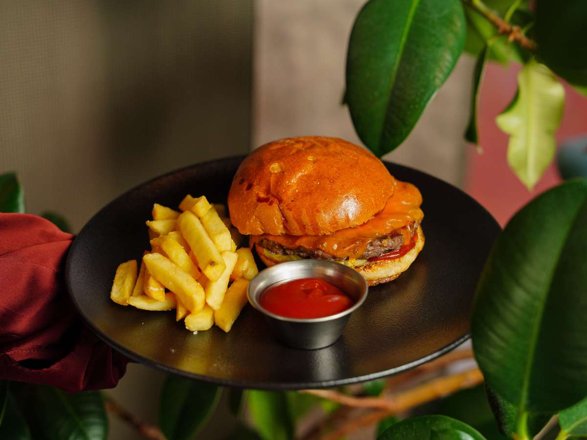 Close-up of a juicy burger with crispy fries and ketchup served on a black plate.
