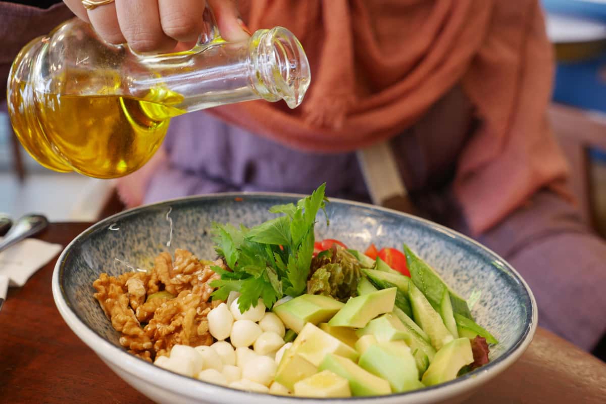 Fresh salad with walnuts, avocado, quail eggs, parsley, and olive oil being poured.