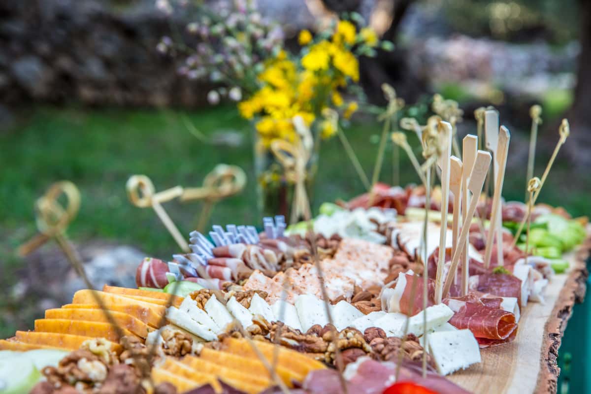 A beautifully arranged charcuterie board with cheese, meats, and nuts, set outdoors in a garden.
