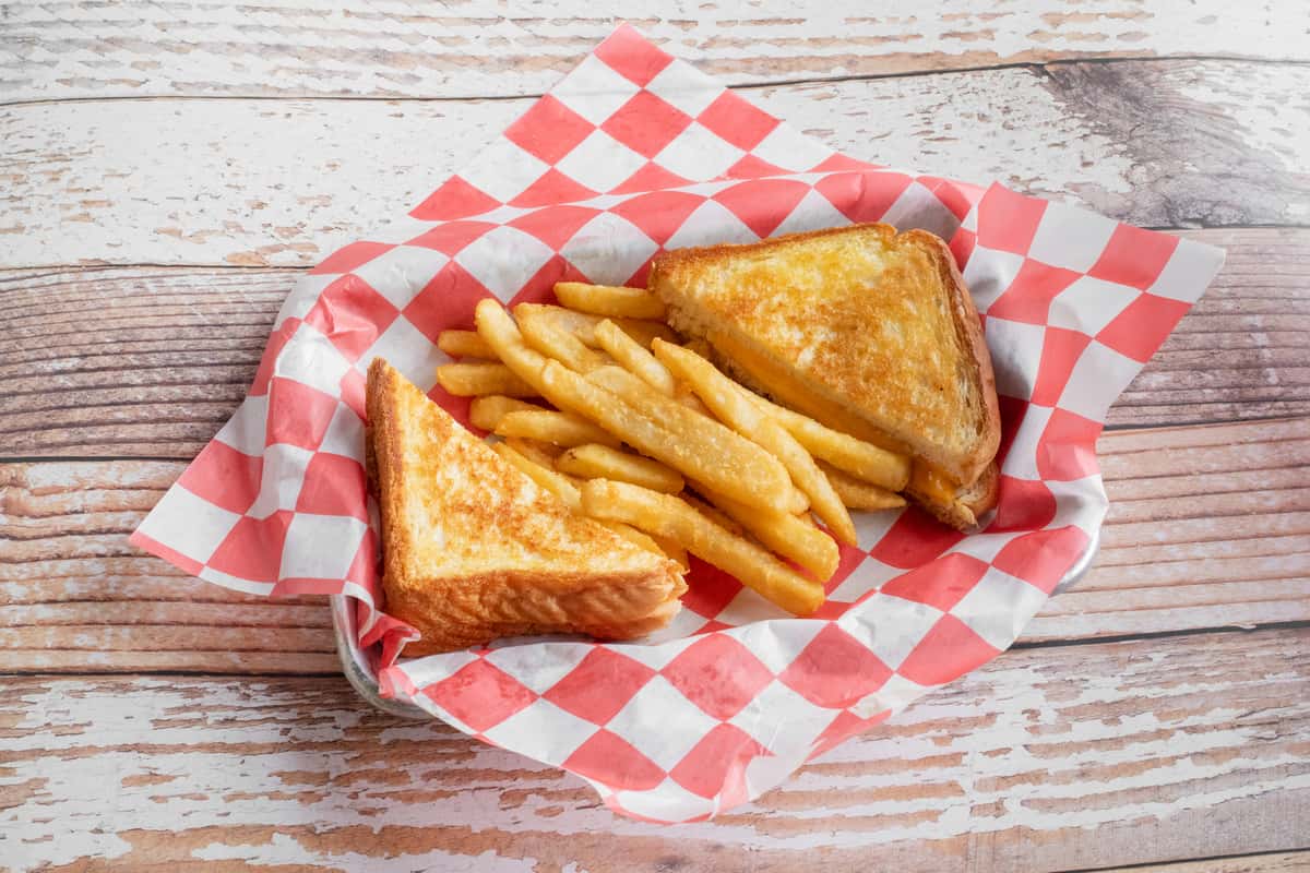 A golden grilled cheese sandwich served with crispy french fries on red and white checkered paper