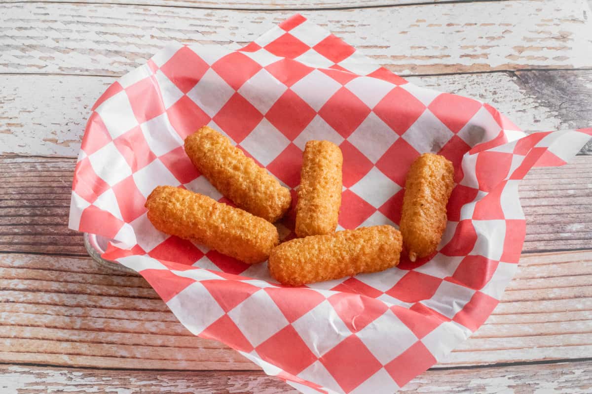 Golden fried mozzarella cheese sticks served on red and white checkered paper