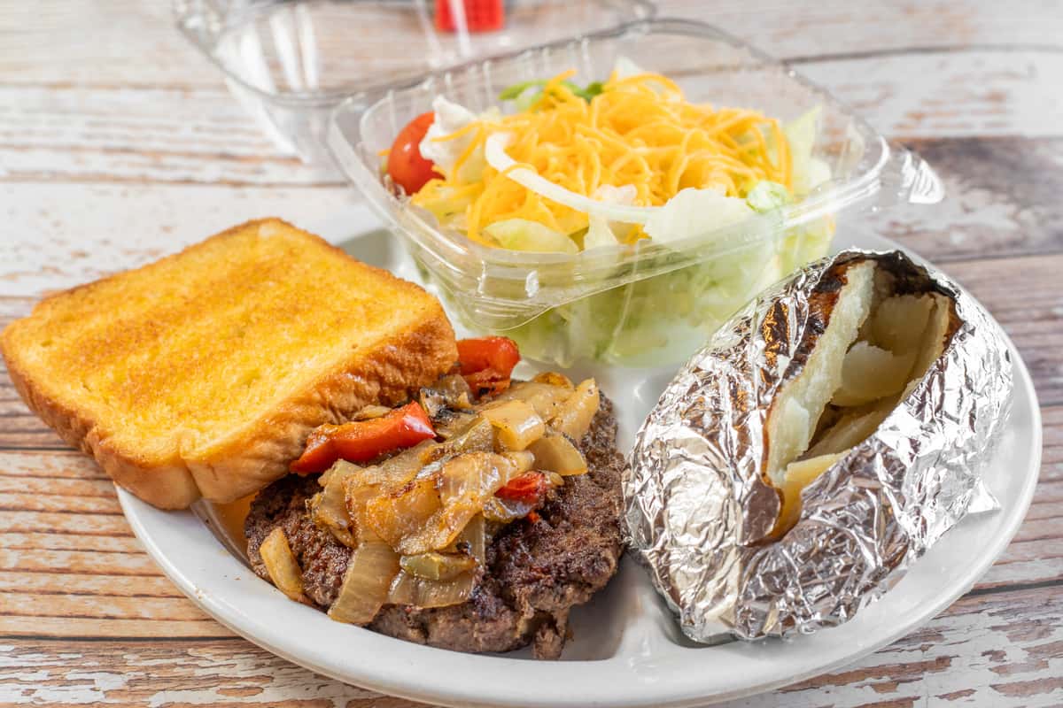 Chopped steak plate topped with grilled onions and peppers, served with Texas toast, a baked potato, and a fresh garden salad.