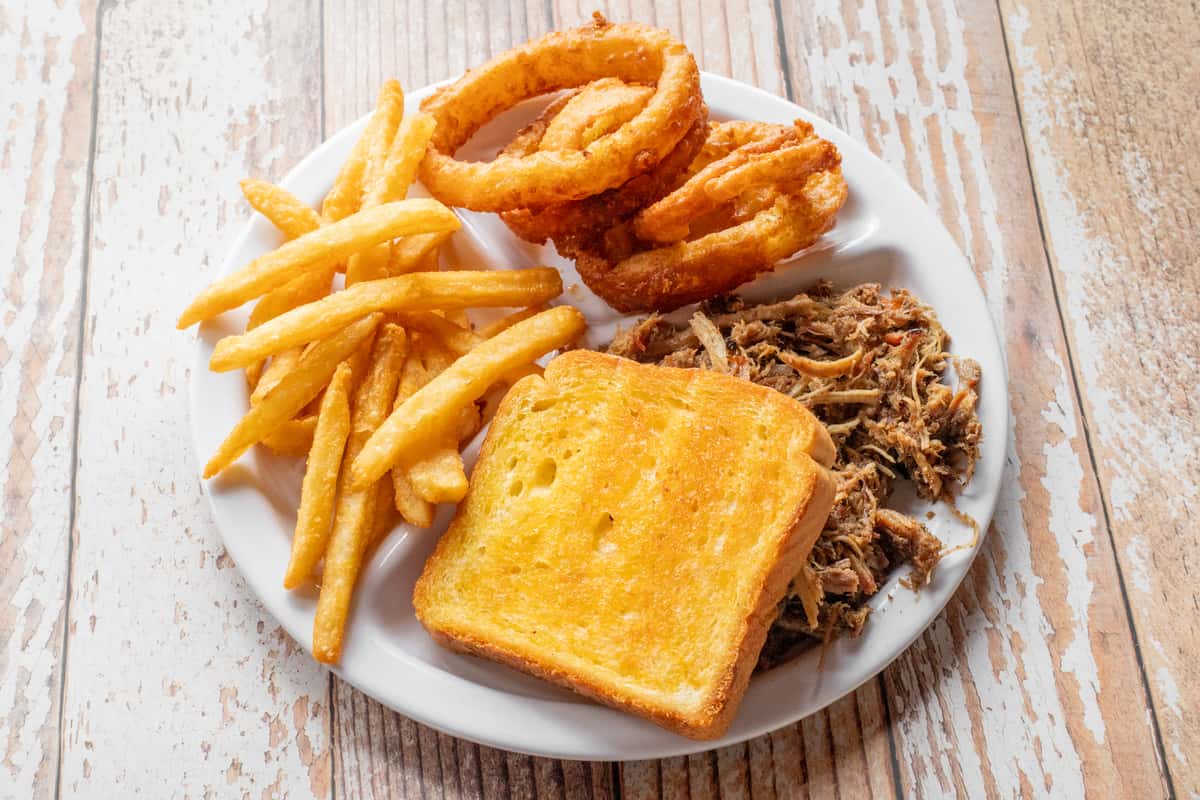 A BBQ plate featuring pulled smoked meat, golden french fries, and a slice of cornbread served on a white plate
