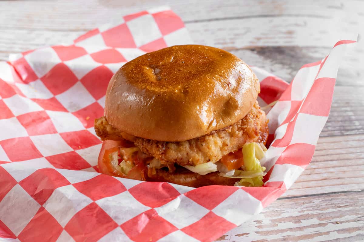 A crispy fried chicken sandwich with toppings on a toasted bun, served on red and white checkered paper