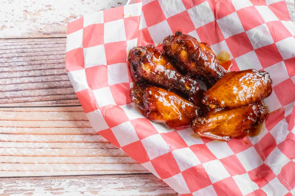 Glazed smoked chicken wings served on red and white checkered paper on a wooden surface