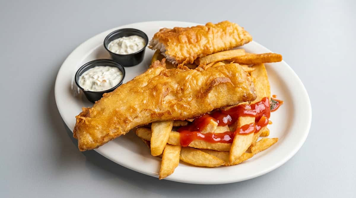Fish and chips with ketchup and two small cups of tartar sauce on a white plate.