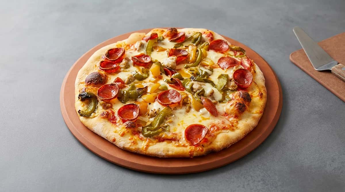 Pizza with pepperoni, green and yellow peppers, sausage, and melted cheese on a wooden peel.