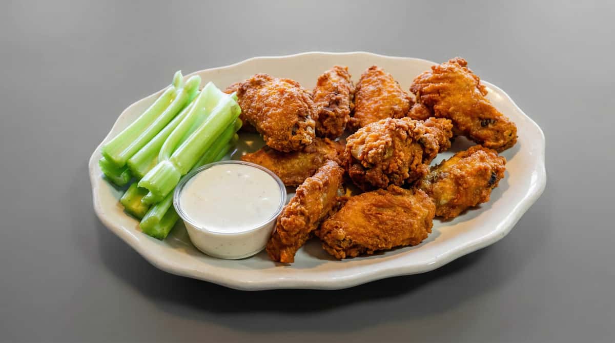 Plate of crispy fried chicken wings with celery sticks and ranch dipping sauce