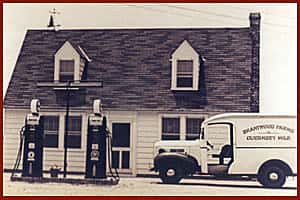 Old black and white image of white truck, house, gas pumps