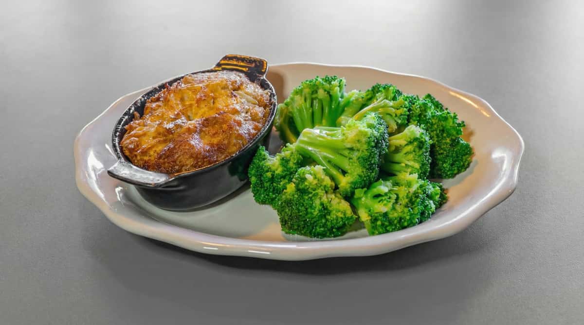 Cheesy baked casserole in a skillet served with steamed broccoli florets