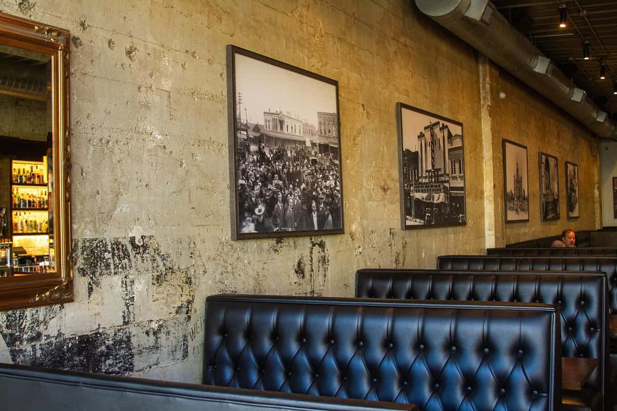 Exposed brick wall with vintage photos and black leather booths in a warmly lit, industrial-style restaurant interior.