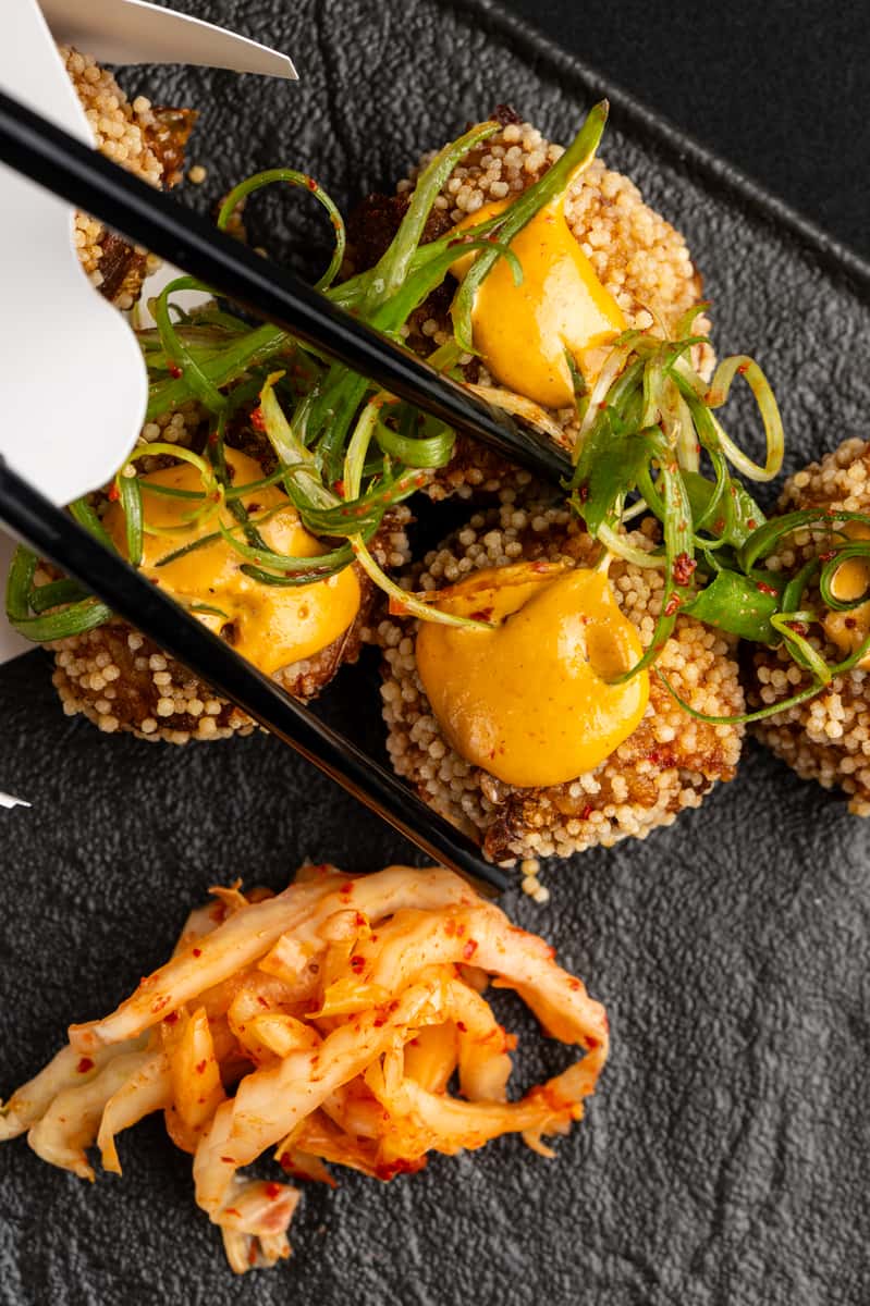 Crispy Asian-style cauliflower bites topped with spicy aioli and scallions served with kimchi and chopsticks