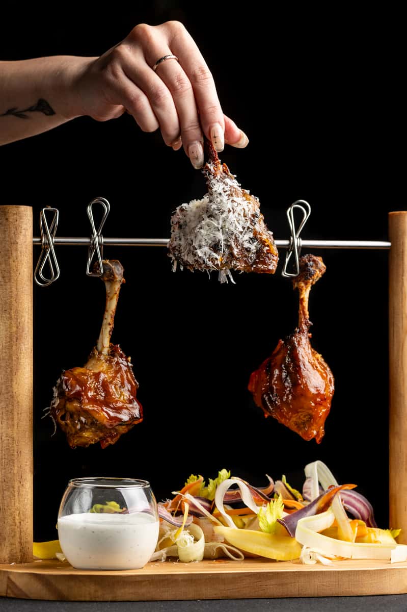 Gourmet glazed chicken lollipops topped with shaved parmesan served on a hanging display with fresh vegetables and dipping sauce