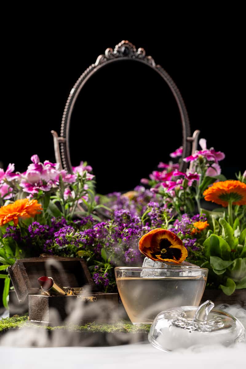 Moody floral cocktail display with smoky dry ice effects, edible flowers, and elegant glassware for a themed restaurant event