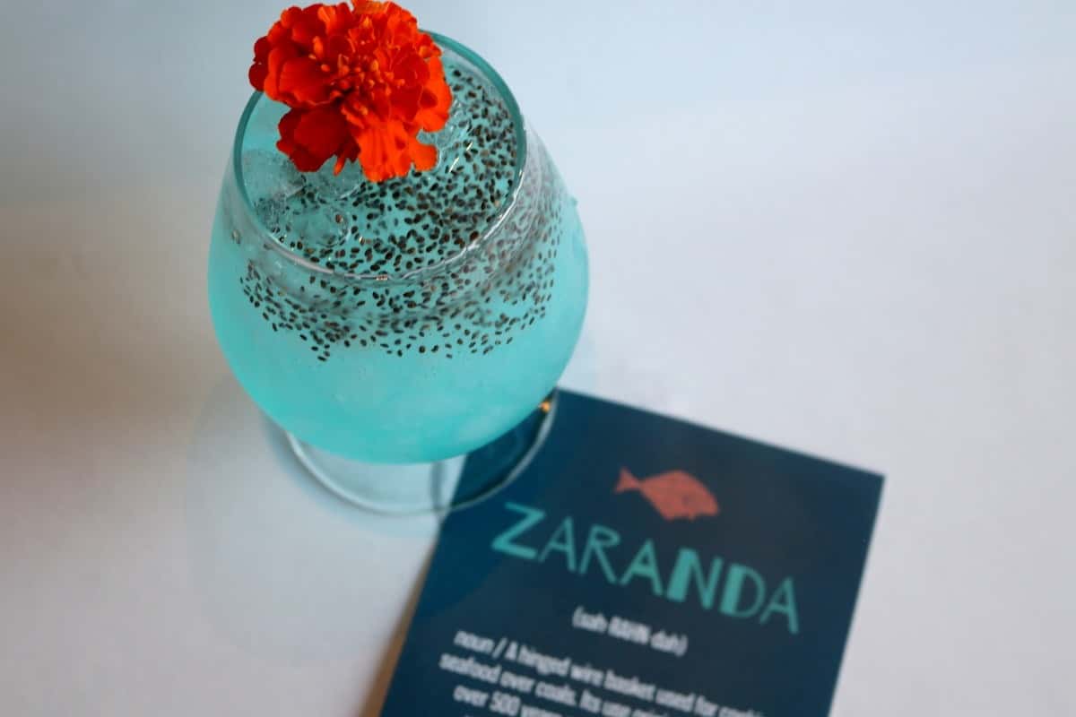 Signature craft cocktail garnished with a red flower, served alongside a Zaranda business card, a creative drink from Zaranda Houston's bar menu