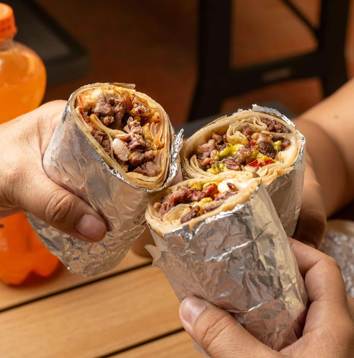 Three foil-wrapped burritos are held aloft for a celebratory cheers at The Salty Rim, a fun beach restaurant.