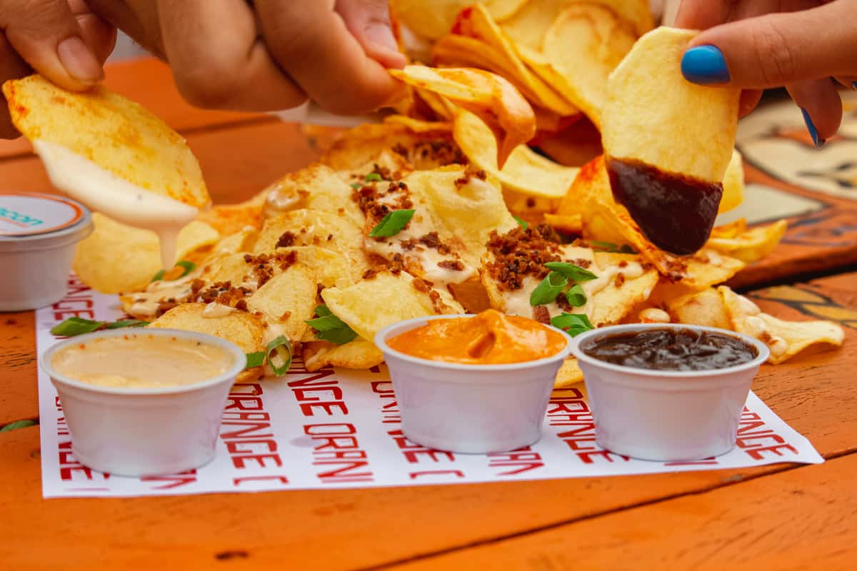 Hands dipping chips into various sauces, alongside loaded chips with toppings, at The Salty Rim, a fun beach restaurant.