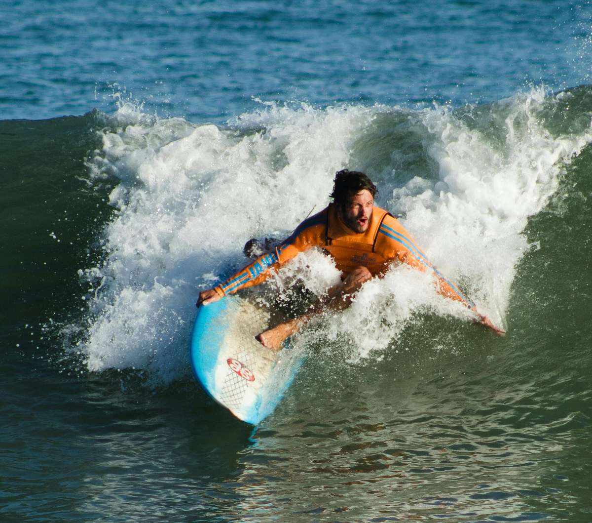 A surfer in an orange wetsuit rides a wave near The Salty Rim, a fun beach restaurant.