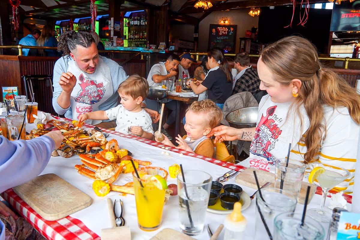 Photo of a family of four, husband and wife, plus two small children sitting on the same side of the table with a Seafeast spread about.