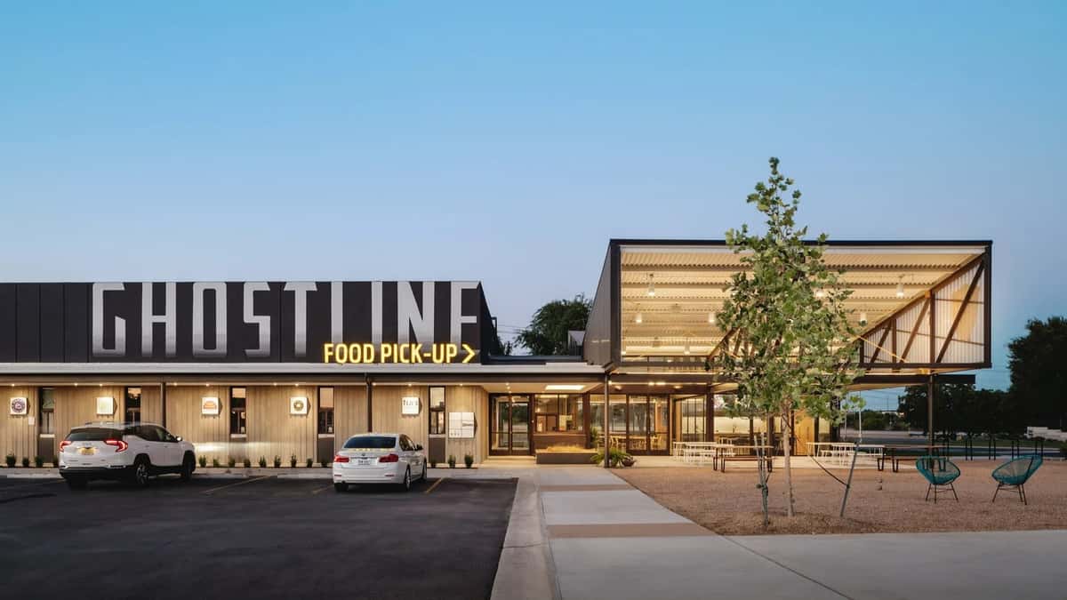 Modern restaurant exterior with "ghost kitchen" food pickup signage, featuring contemporary architecture, outdoor seating, and a clean, minimalist dining atmosphere at dusk.