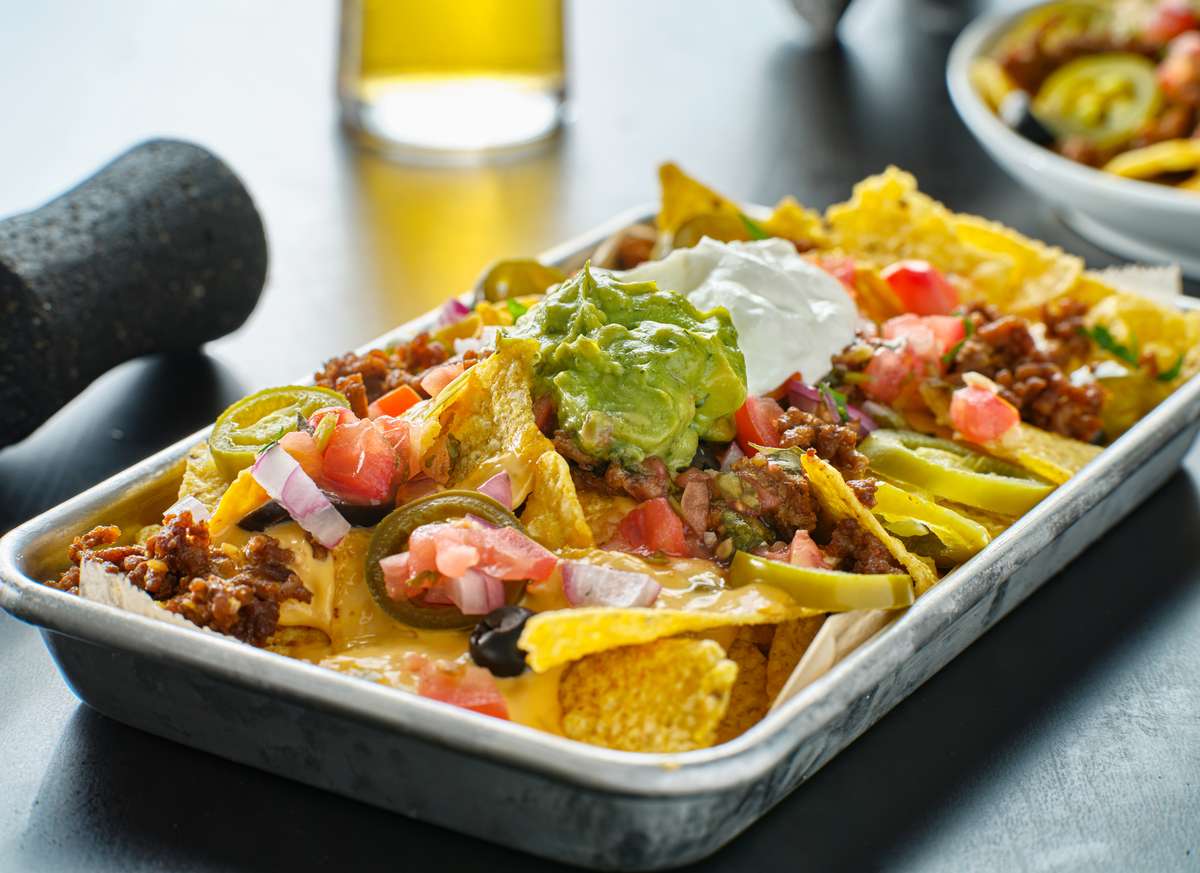 Loaded beef nachos with melted cheese, seasoned ground beef, guacamole, sour cream, jalapeños, and fresh pico de gallo on a rustic Mexican restaurant platter.