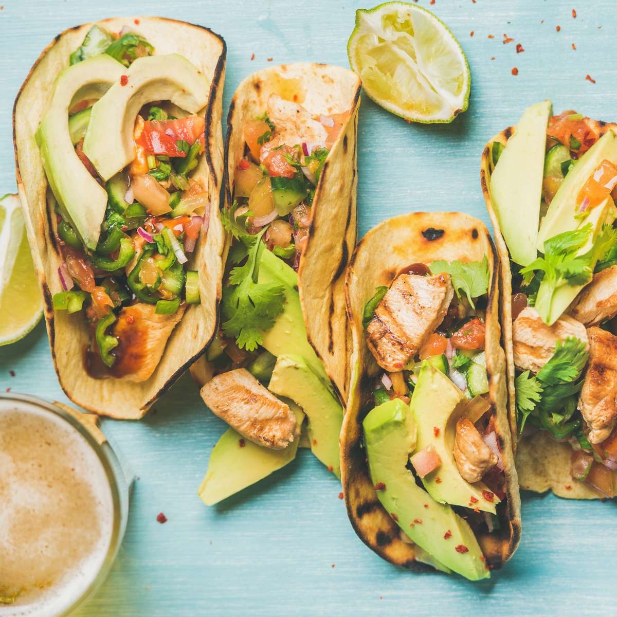 Grilled chicken tacos with avocado slices, fresh pico de gallo, and cilantro in charred corn tortillas, served with lime wedges on a vibrant Mexican restaurant table.
