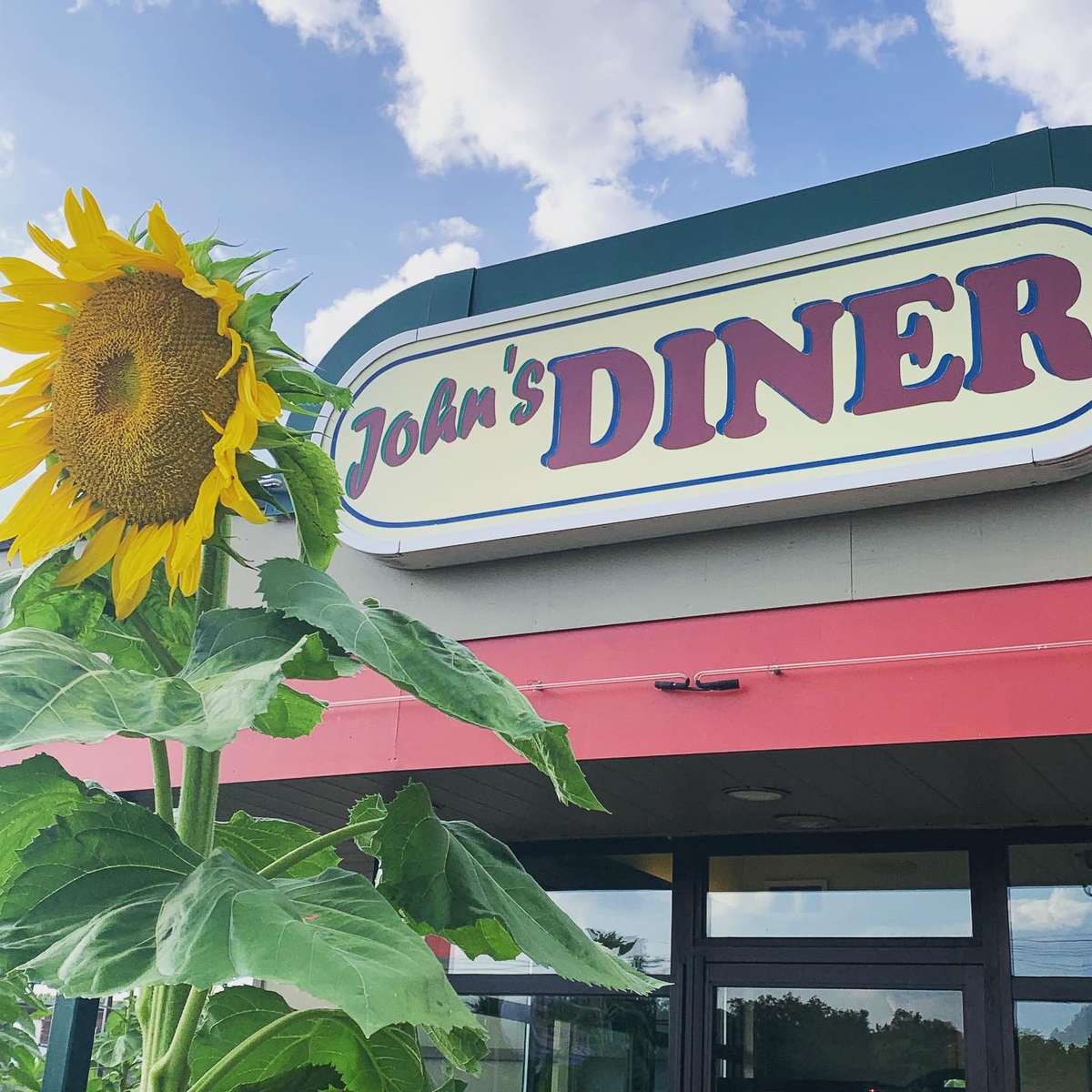 Exterior of John's Diner with the sign, a blue sky with clouds and a sunflower