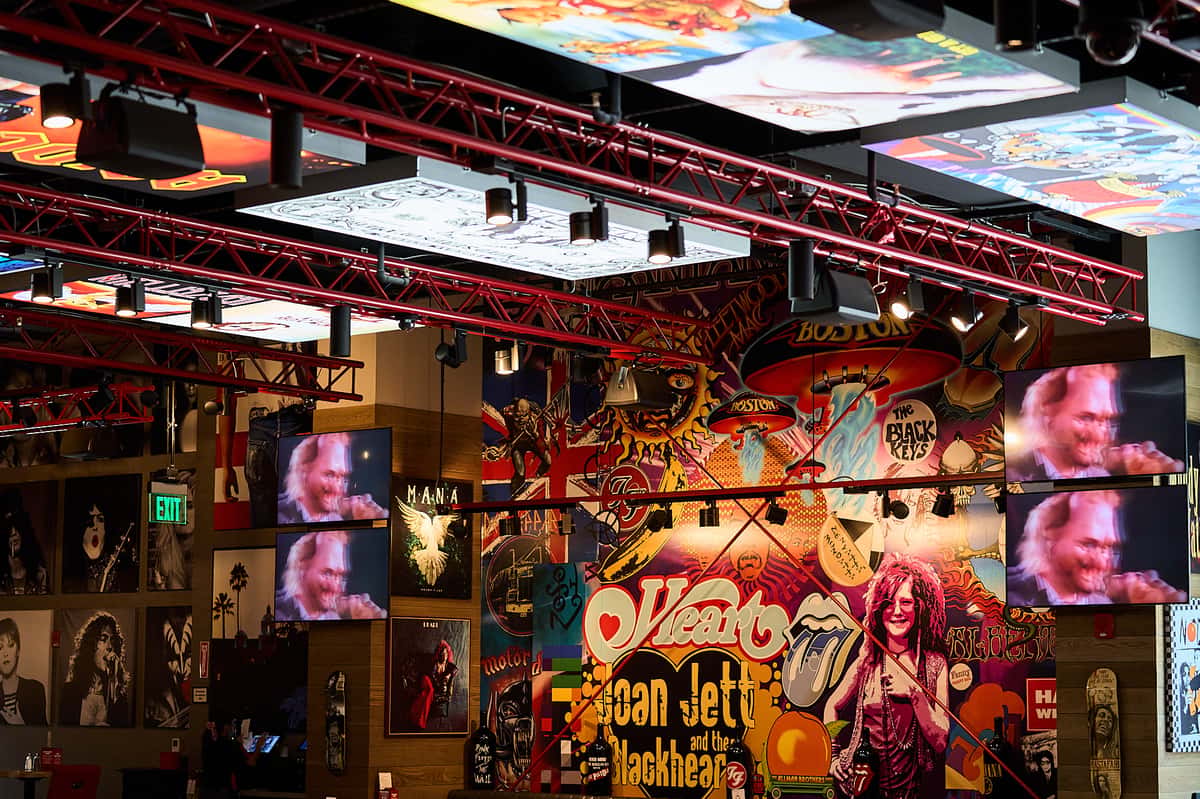 Interior of a Rock & Brews restaurant inside Rolling Hills Casino featuring colorful rock music murals, concert imagery, multiple TV screens, and red overhead lighting fixtures.