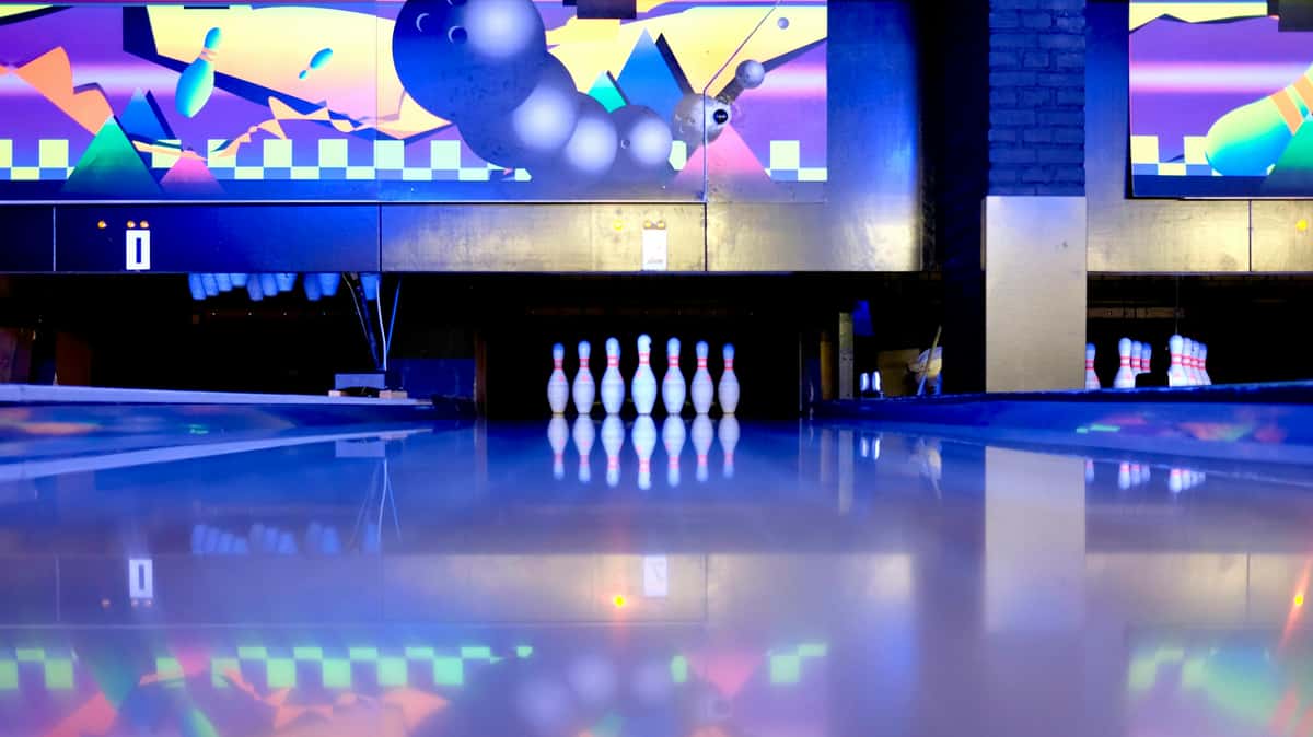 Bowling pins set up under vibrant neon lights with colorful abstract graphics above the lane.