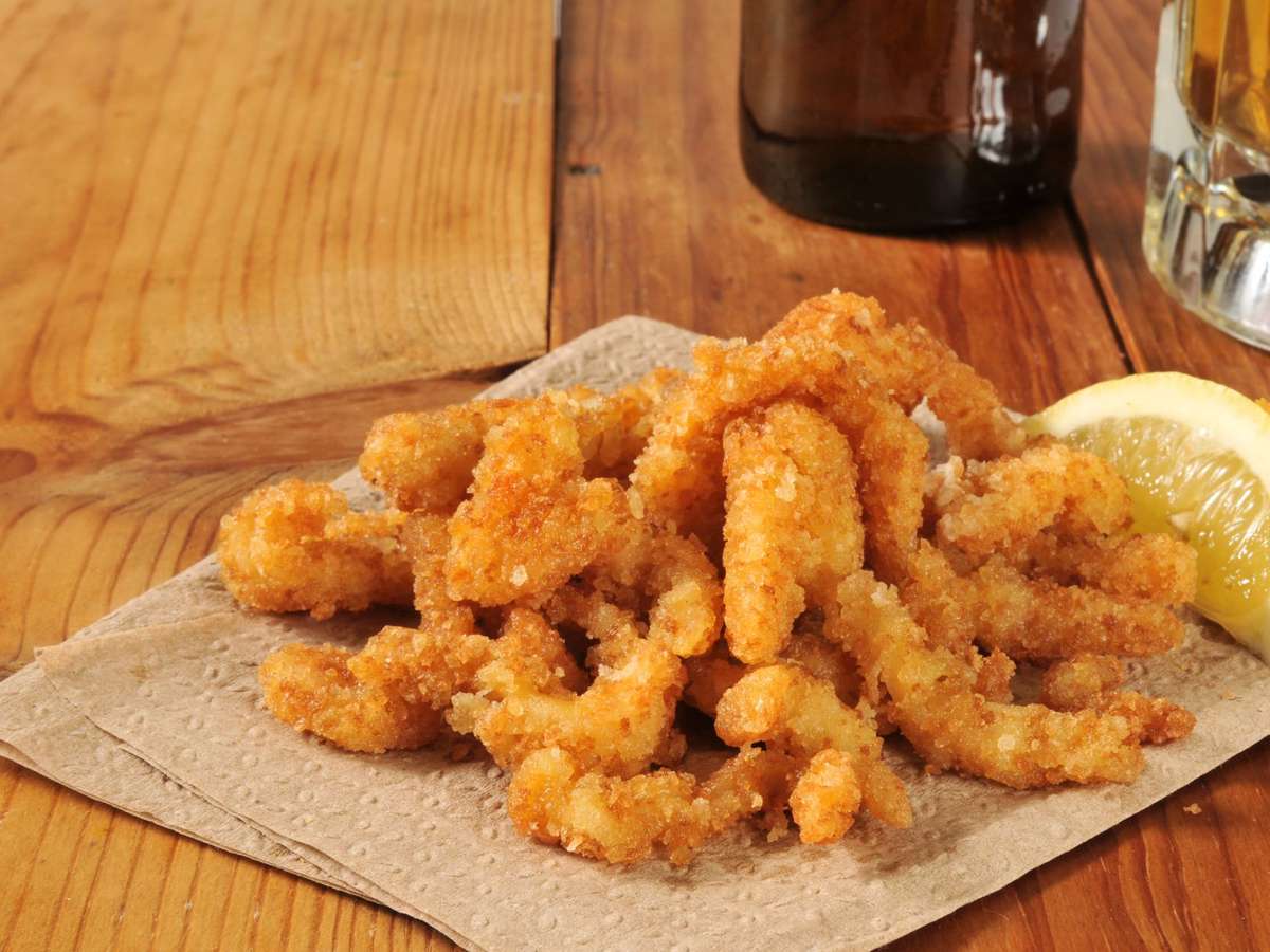 Fried clam strips on brown paper with a lemon slice and two glass bottles in the background on a wooden table