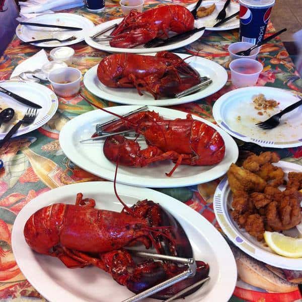 Plates of cooked full lobsters on a table with a plate of mixed fried seafood and lemon next to other empty plates with forks