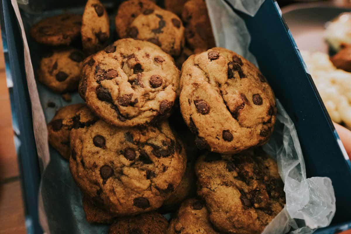 Freshly baked chocolate chip cookies stacked inside a paper-lined box.