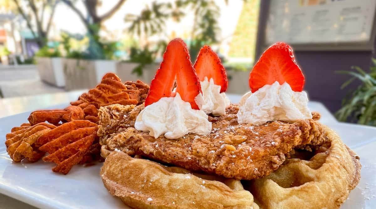 Chicken and waffles with three strawberry slices, whipped cream, and sweet potato waffle fries.