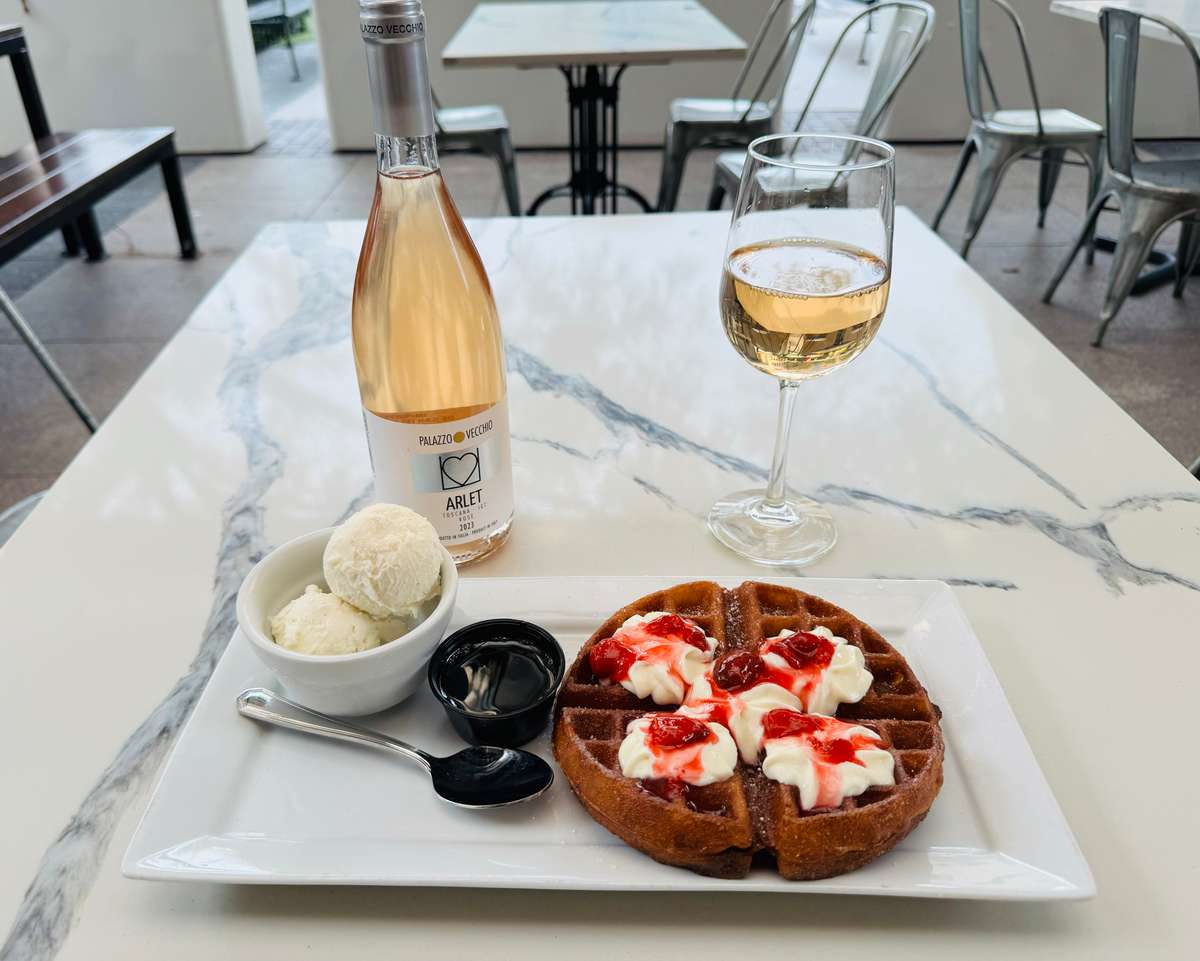 Churro style Belgian waffle topped with whipped cheesecake, strawberry topping and powered sugar served with ice cream