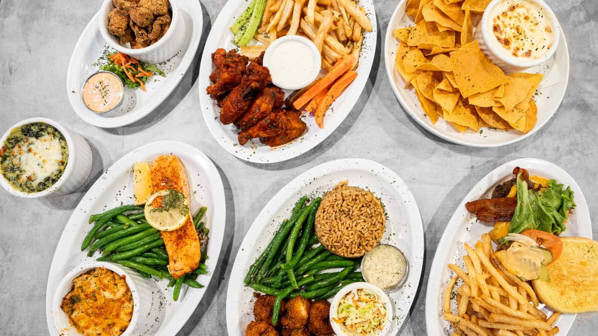 A vibrant Coaches Corner menu spread showcasing diverse American comfort foods like buffalo wings, grilled salmon, burgers, crispy fries, and various appetizers and dips on white plates.